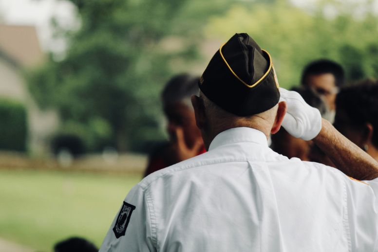 An older veteran in a white uniform salutes. The veteran's back is to the camera and we do not see their face.