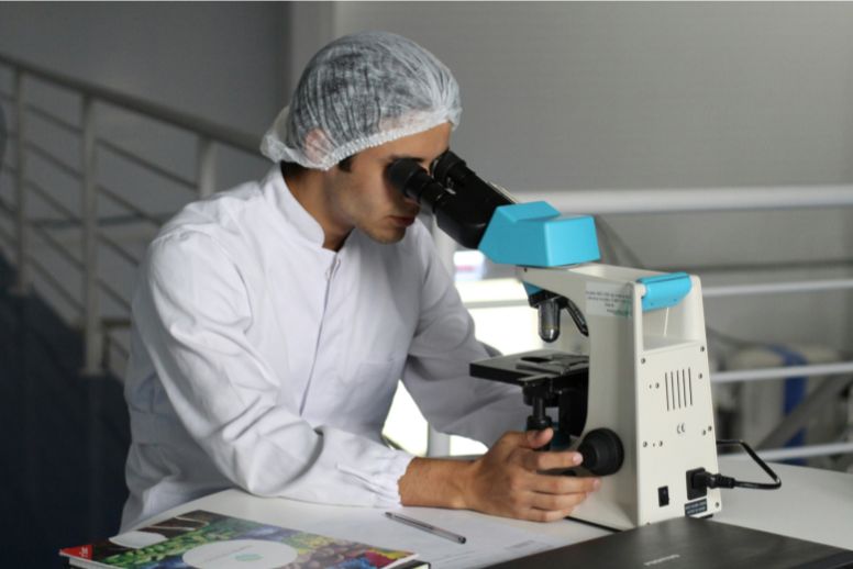 A researcher wearing a hair net looks into a microscope. This illustrative photo accompanies a January 2024 national news roundup, including a story about medical cannabis research funding.