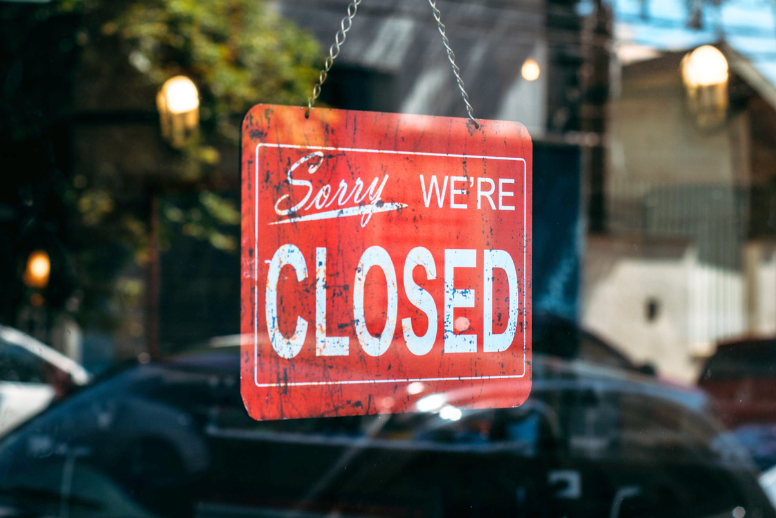 A red sign that says "sorry, we're closed" hangs in the window of a storefront.