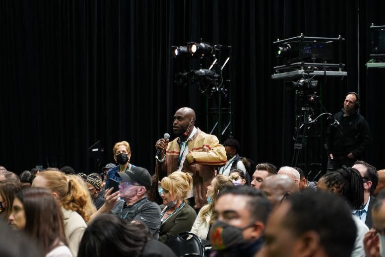 A conference attendee in a brown jacket stands among a crowd to address a speaker during a session at CWCBExpo.