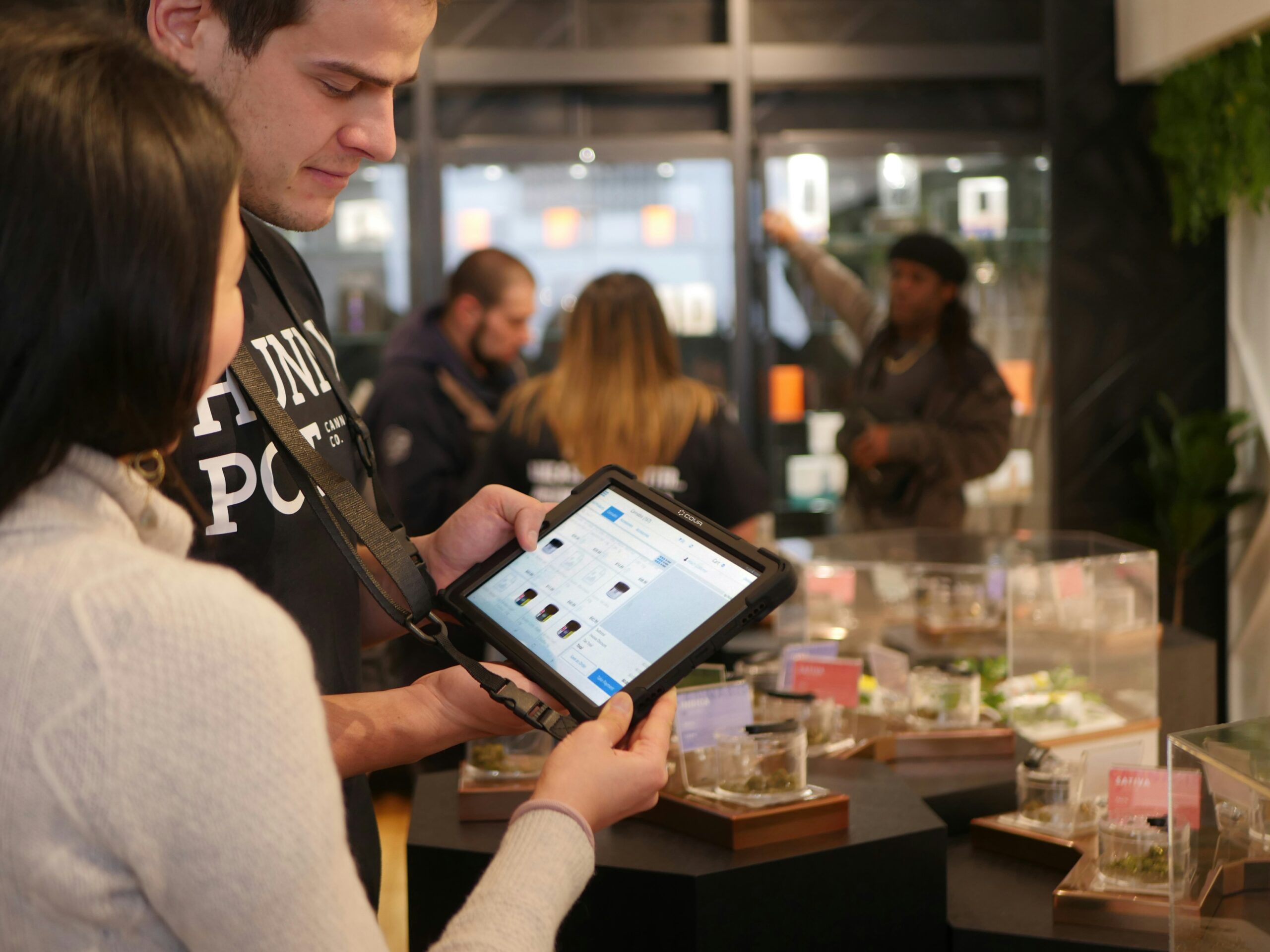 Two people inside a dispensary look at a tablet for ordering cannabis. This illustrates the record 4/20 sales seen across the nation in 2024.